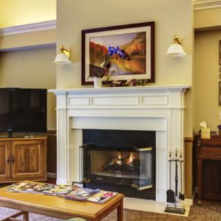 A cozy living room featuring a fireplace with a painting above, and a seating area.