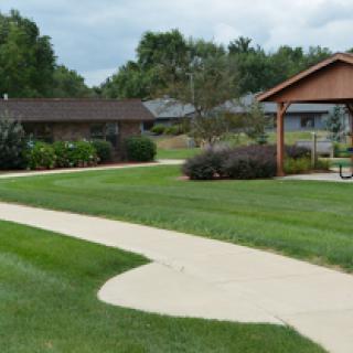 A serene park scene featuring a winding pathway and well-maintained grass, with buildings in the background.