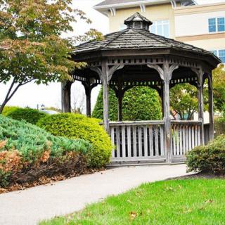 A charming wooden gazebo surrounded by lush greenery and a tidy walkway.