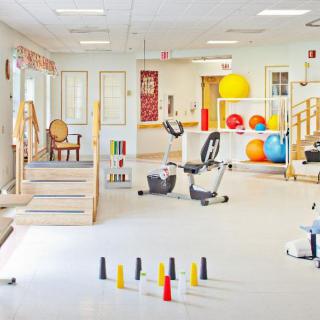 A well-equipped physical therapy room with various exercise machines and therapy tools, including bicycles and therapy balls.