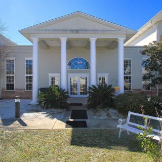 A building with large columns at the entrance, surrounded by landscaping on a sunny day.