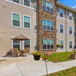 A residential apartment building exterior with an outdoor patio, featuring chairs, a table, and an umbrella.