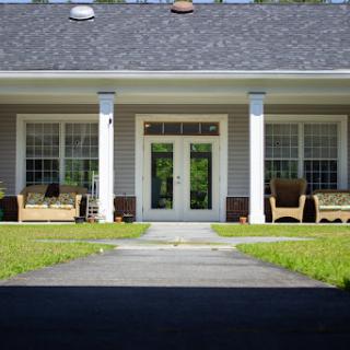 A welcoming entrance to a charming house with a well-maintained lawn and outdoor seating.