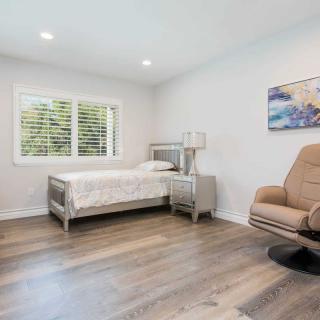 A minimalist bedroom with a single bed, armchair, and wall art.