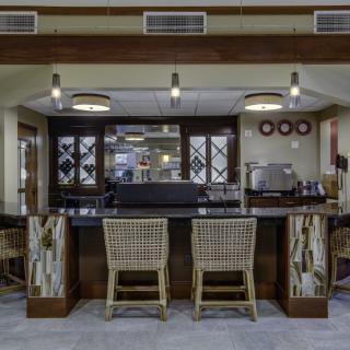 A stylish bar area featuring a dark countertop, wicker chairs, and modern lighting.