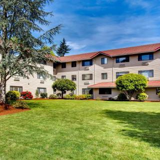 A residential apartment building with well-maintained lawns and surrounding trees under a clear blue sky.