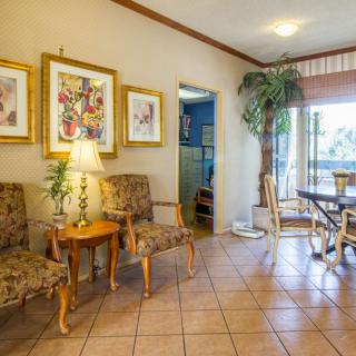 A cozy living space with ornate chairs, a lamp on a side table, framed artwork on the wall, and an indoor plant near a dining area.