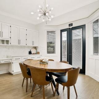 A modern dining room featuring a round wooden table and stylish chairs, illuminated by a contemporary chandelier.