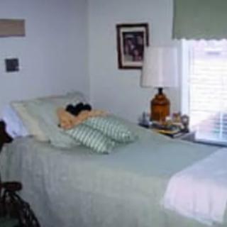 A cozy bedroom with a neatly made bed, featuring decorative pillows and a bedside lamp next to a window.