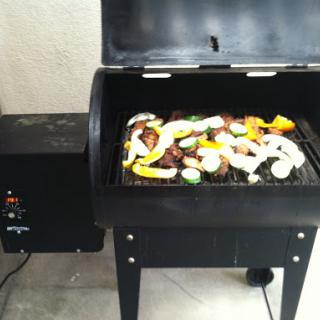 A black grill is set up outdoors, featuring a variety of colorful vegetables being cooked.