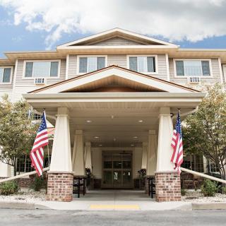 The entrance of a building adorned with American flags, surrounded by trees under a partly cloudy sky.