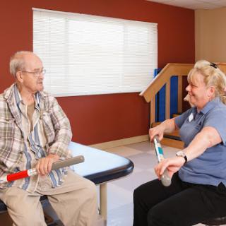 A healthcare worker assists an elderly man with exercises during a physical therapy session.