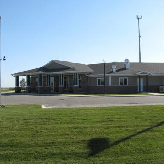 A single-story building with a parking area and a well-maintained lawn under a clear blue sky.