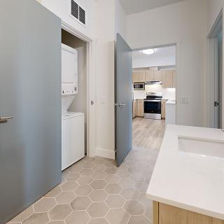 Modern interior with a laundry area and kitchen visible from the hallway.