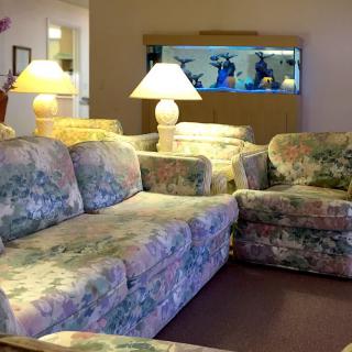 A cozy living room setup featuring floral-patterned sofas, glowing lamps, and a large fish tank.