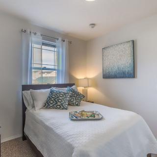 A modern and minimalist bedroom with a neatly made bed, decorative pillows, a lamp, and an abstract artwork on the wall.
