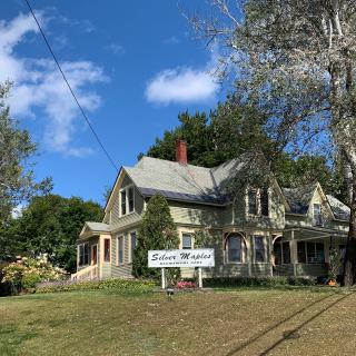 A charming Victorian-style house with a sign in front, surrounded by trees and under a clear blue sky.