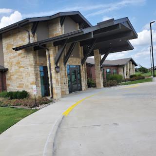 A modern stone-clad building with a covered entrance and landscaped surroundings.