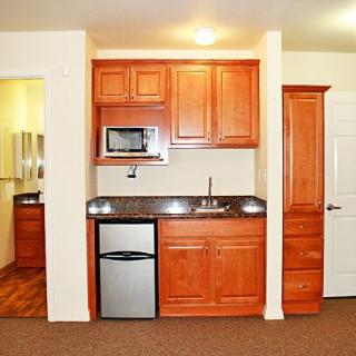 A compact kitchenette with wooden cabinets, a sink, microwave, and mini fridge.