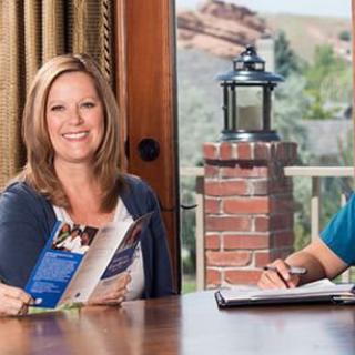 Two women sitting at a table, one reading a brochure and the other writing in a notebook.