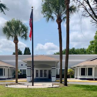 A building entrance with a flagpole and palm trees in the foreground.