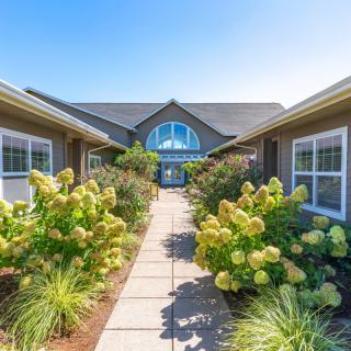 A well-maintained pathway leading to a residential house, surrounded by lush gardens and beautiful flowers.