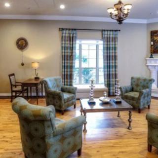 A cozy living room with armchairs arranged around a coffee table, featuring elegant furnishings and natural light from a large window.