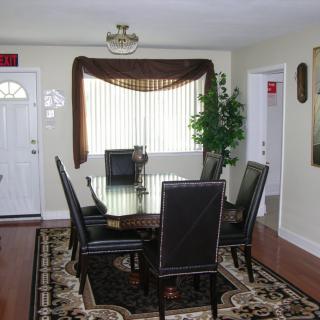 A cozy dining room with a table set and chairs, featuring elegant curtains and a decorative plant by the window.