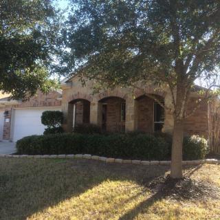 A brick house with a well-maintained front yard and trees, partially shadowed by sunlight.