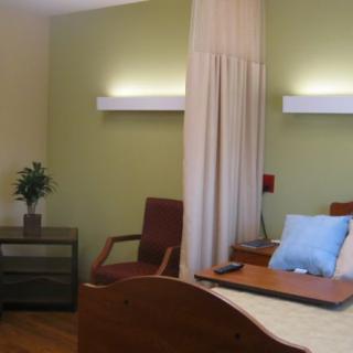 A well-lit hospital room with a bed, chair, and a small table with a plant for decoration.