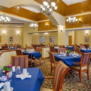 An elegant dining area with blue tablecloths, wooden chairs, and overhead chandeliers.