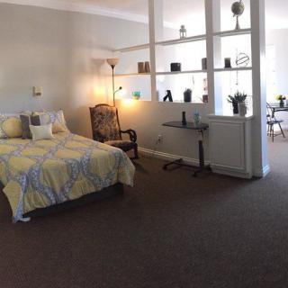 A cozy bedroom with a bed, armchair, and decorative shelves featuring various plants and ornaments.