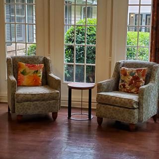 A cozy living room corner with two armchairs, decorative pillows, and a small side table by a window.
