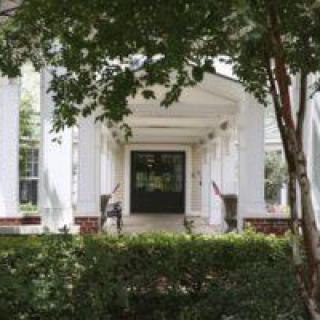 A view of a building entrance with white columns and a surrounding garden.