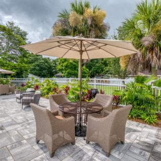 A serene patio area with wicker chairs and a table under a large umbrella, surrounded by lush greenery.