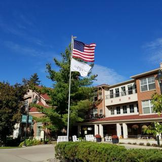 A building with an American flag flying on a flagpole surrounded by trees under a clear blue sky.