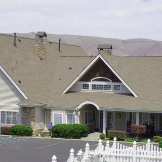 A residential-style building with a steep roof, multiple chimneys, and a white picket fence set against a mountainous backdrop.