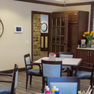 A cozy dining area featuring a table with chairs, a cabinet, and decorative elements including flowers and a wall clock.