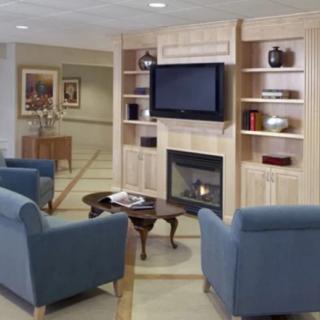 A cozy living room with blue armchairs, a wooden fireplace, and a television mounted on shelves.