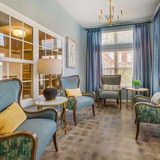 A cozy living room with elegant chairs, blue curtains, and a chandelier.
