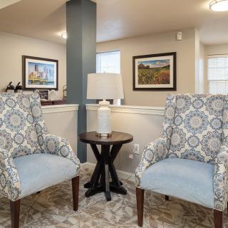 A cozy living room corner with patterned chairs and a small table with a lamp.