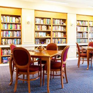 A cozy library with wooden tables and chairs, surrounded by shelves filled with books.