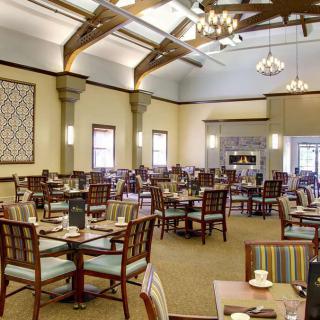 An elegant dining room with neatly arranged tables and chairs, featuring chandeliers and wooden ceiling beams.