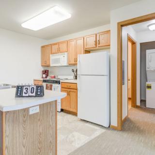 A modern apartment kitchen with wooden cabinets and white appliances.