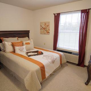 A cozy bedroom with a neatly made bed, stylish decor, and a window with red curtains.