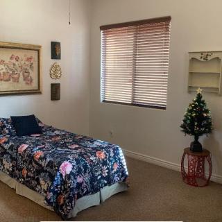 A cozy bedroom featuring a single bed with floral bedding, wall art, and a small Christmas tree by the window.