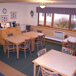 A cozy dining room with tables and chairs arranged neatly, featuring large windows and a cabinet.
