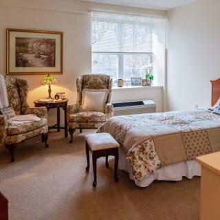A cozy bedroom with an elegant interior design featuring a bed, two chairs, and a window providing natural light.