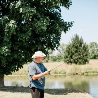 A man enjoying a peaceful day of fishing by the pond under the shade of a tree.