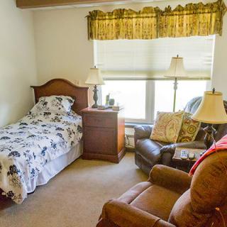 A cozy bedroom with a single bed, armchairs, and lamps near a window.